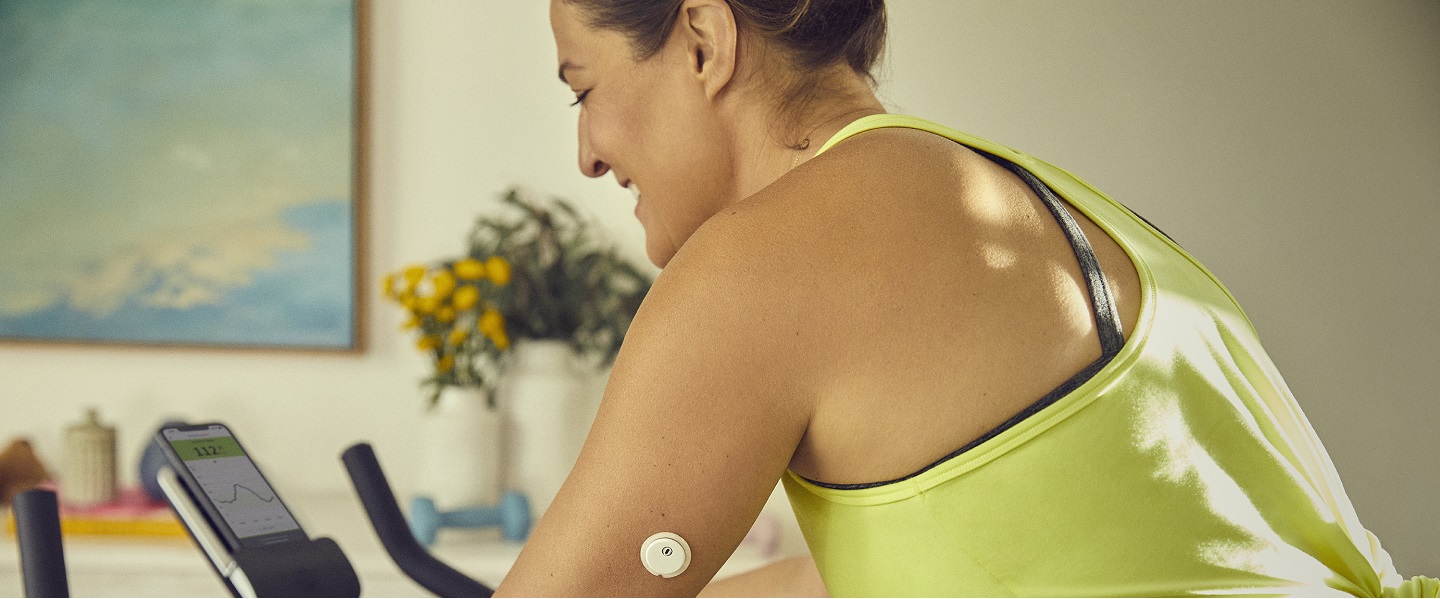 Eine Frau mit FreeStyle Libre 3 Sensor am Oberam sitzt auf einem Ergometer