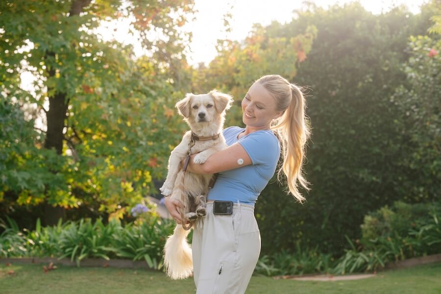 Junge Frau mit Libre Sensor am Arm spiel mit Hund im Garten