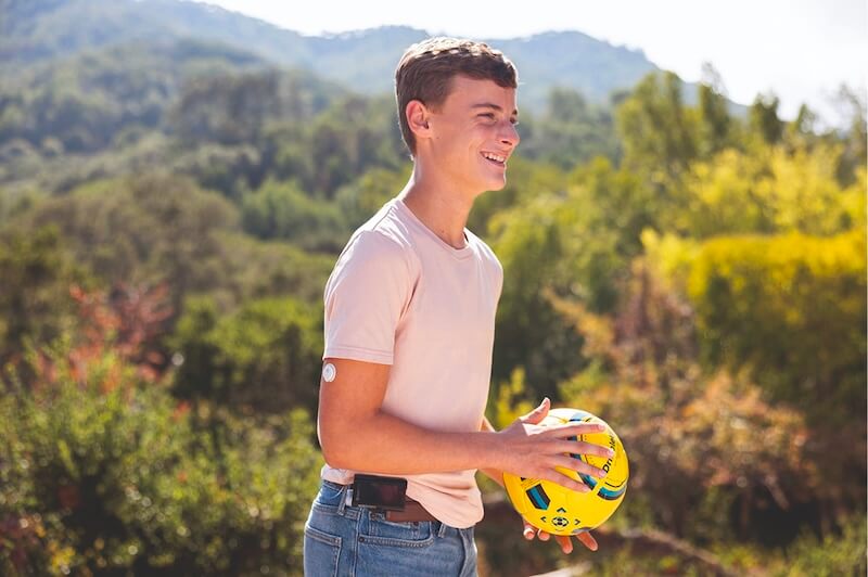 Jugendlicher mit einer Insulinpumpe und FreeStyle Libre Sensor spielt mit einem Ball